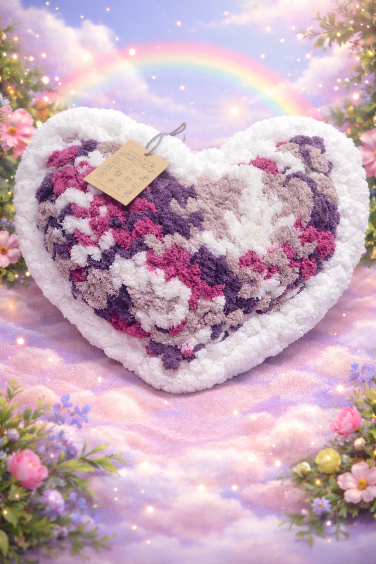 Heart-shaped knitted pillow with a rainbow and flowers in the background